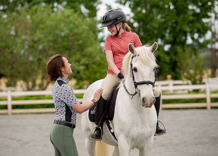 Child on horseback smiling while talking to riding instructor