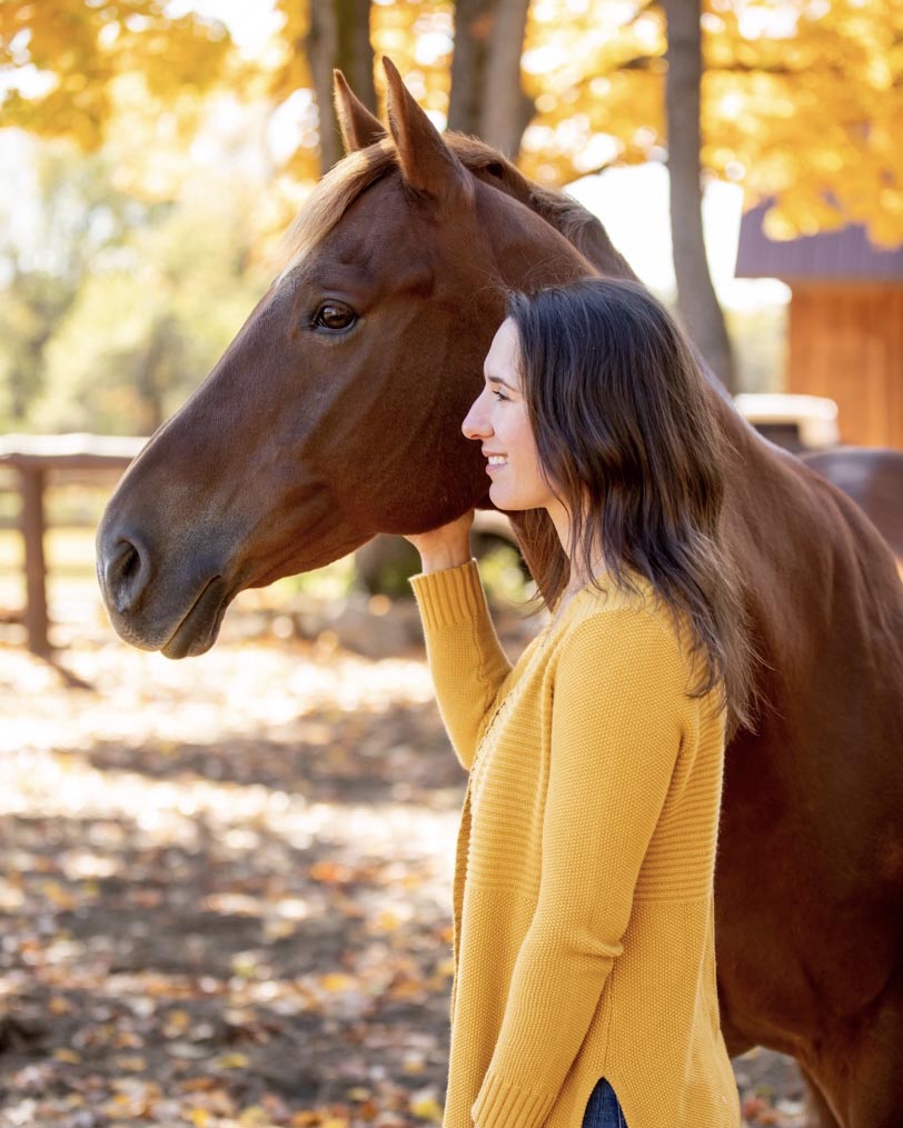 Profile photo of Liz with a chestnut horse against fall foliage